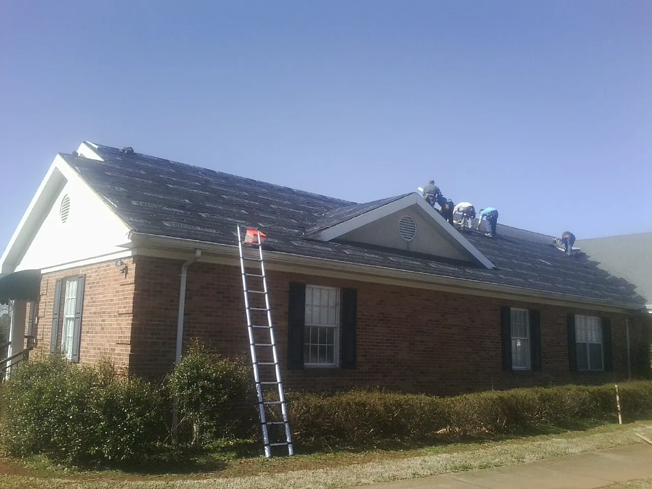 Crew tearing shingles off a brick ranch roof with a ladder set — Emergency Roof Repair work by our crew in Saint Clair