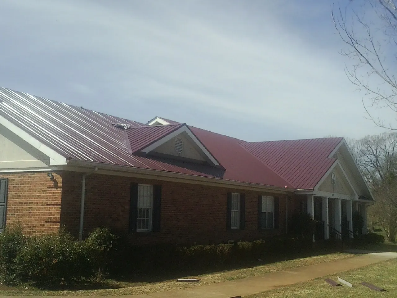 Red metal roof with gabled entries on a long brick building, from a Hail Damage Roof Repair job in Saint Clair